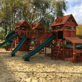 Wooden playground structure with slides and sand area in a park setting